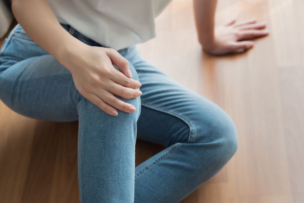 Person sitting on the floor holding their knee in pain after an injury or fall. Person sitting on the floor holding their knee in pain after an injury or fall.