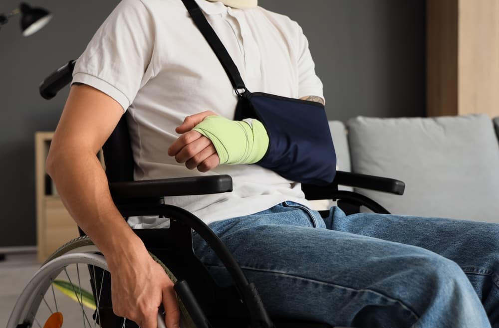 Young man with a broken arm sitting in a wheelchair at home after an accident.