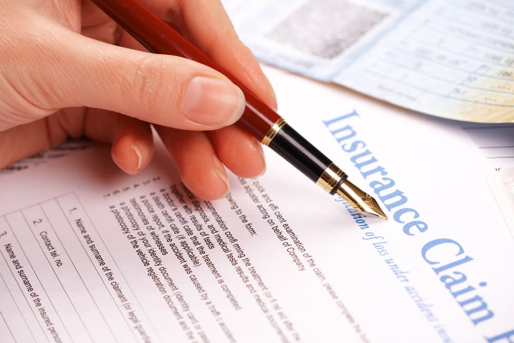 A woman is filling out an insurance claim form by hand, with documents.