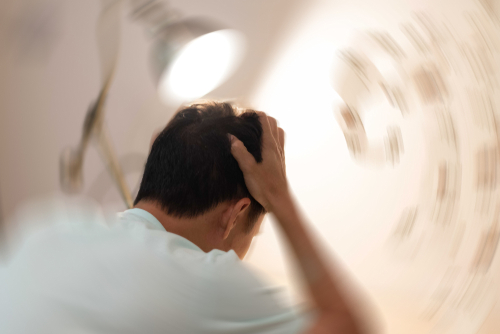 A person holds their head with both hands as the background appears distorted and spinning, symbolizing dizziness or a concussion.