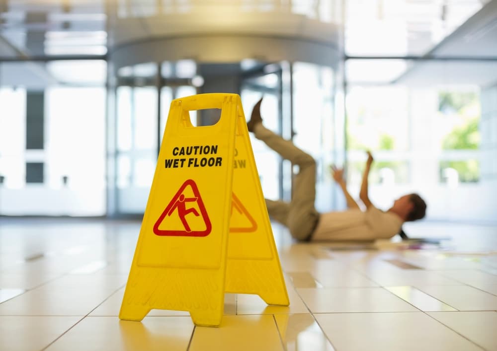 Wet floor caution sign in hallway as man slips and falls in workplace accident. Wet floor caution sign in hallway as man slips and falls in workplace accident.