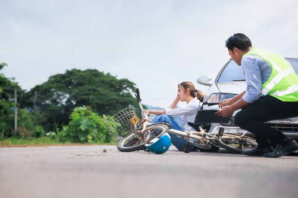 It looks like you want an image description for a vehicle accident scene involving a bicycle and a car, with an insurance officer and an injured cyclist.