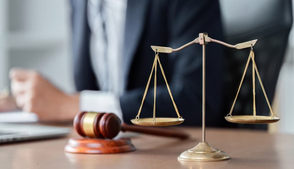 A lawyer reviews legal documents at a desk with scales of justice and a gavel in a modern office setting.