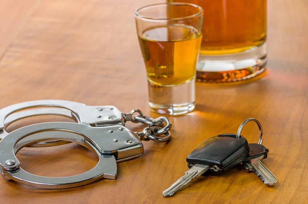A shot glass alongside car keys and handcuffs, symbolizing the consequences of drinking and driving.