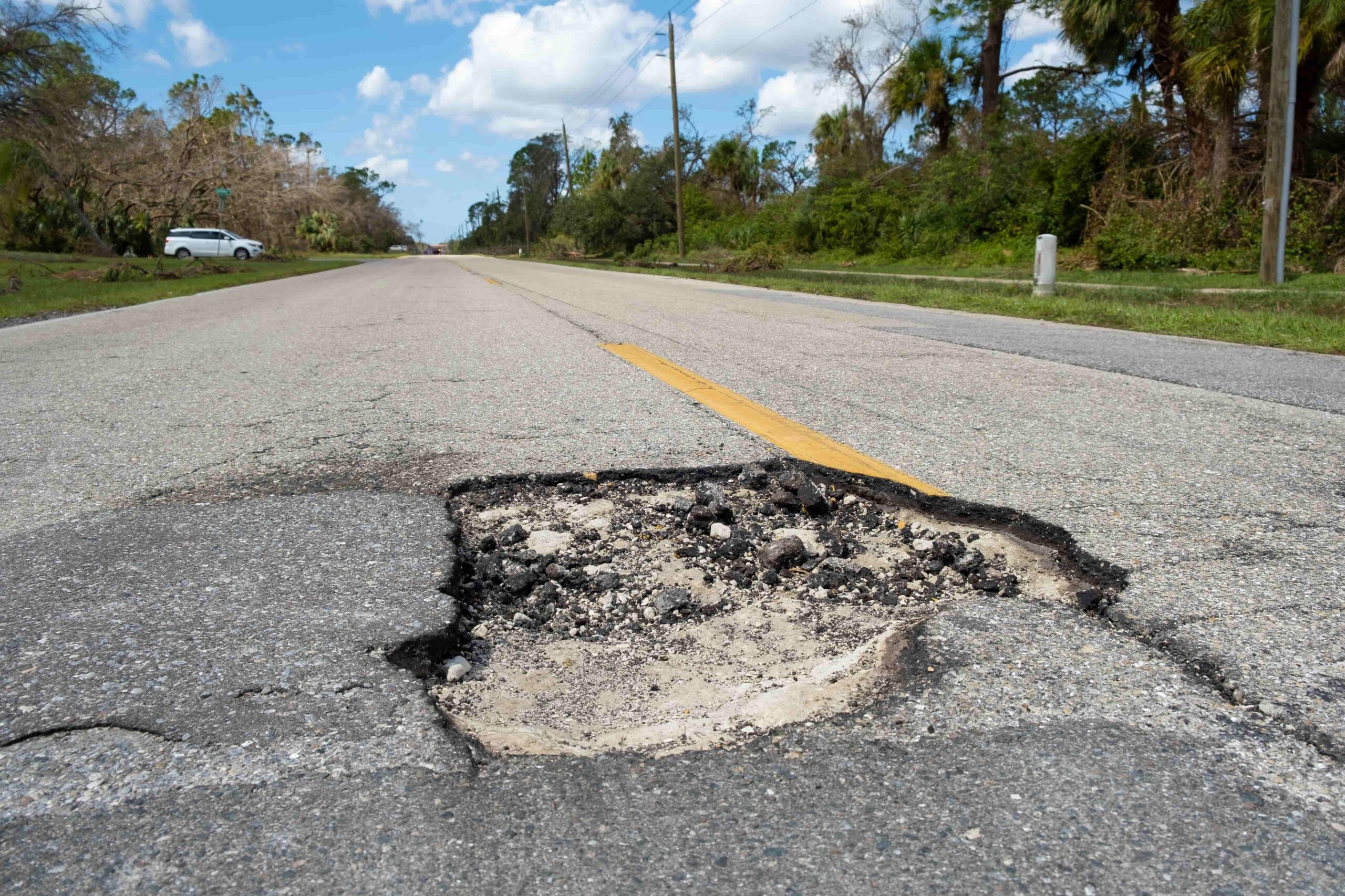 Large pothole in the middle of a roadway creating a dangerous driving hazard and potential accident risk.