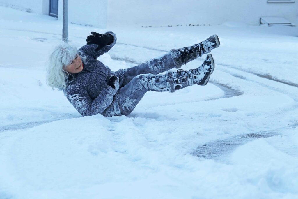 Mujer mayor resbalando y cayendo en una acera con hielo durante condiciones invernales con nieve. Mujer mayor resbalando y cayendo en una acera con hielo durante condiciones invernales con nieve.