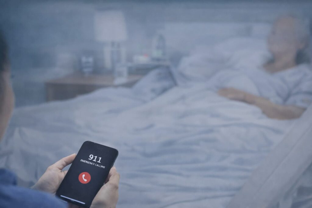Calling 911 to Report Nursing Home Medical Emergency or Neglect in New York Person dialing 911 on smartphone in nursing home room during suspected medical emergency involving elderly resident.