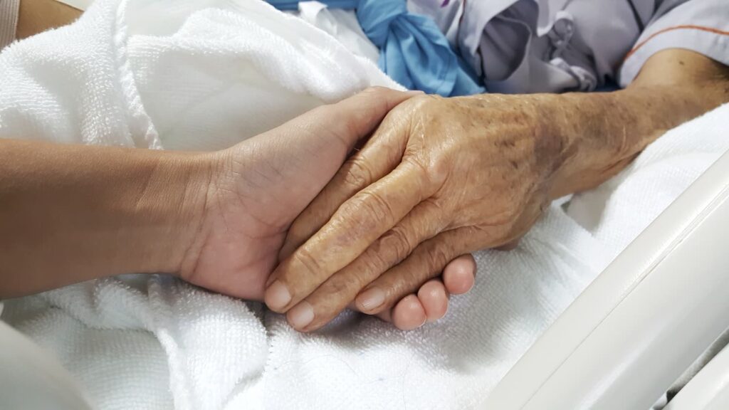 Recognizing Sepsis and Bed Sore Warning Signs in Nursing Home Residents Family member holding elderly nursing home resident’s hand in hospital bed, symbolizing concern about sepsis and bed sore neglect.